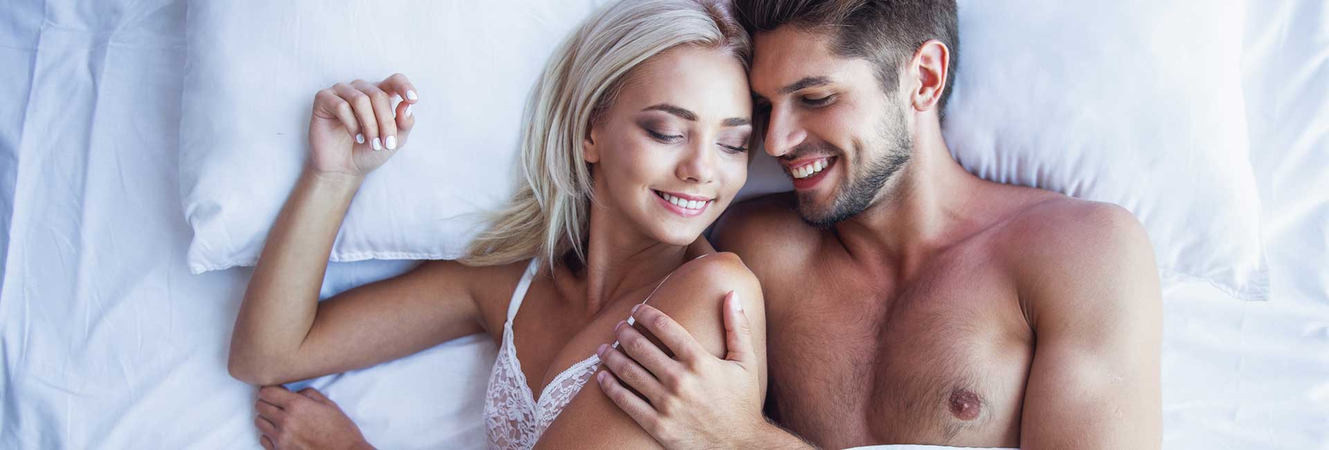 A young couple hugging and smiling while sleeping together in bed.